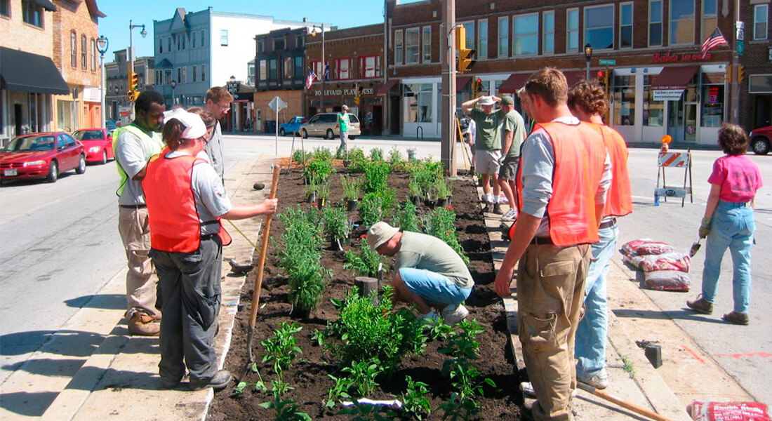 People in orange vests planting small plants in an urban garden