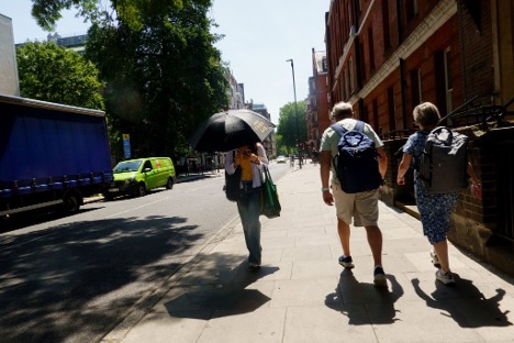 People walking in sunlight while one person holds a umbrella for shadow. 